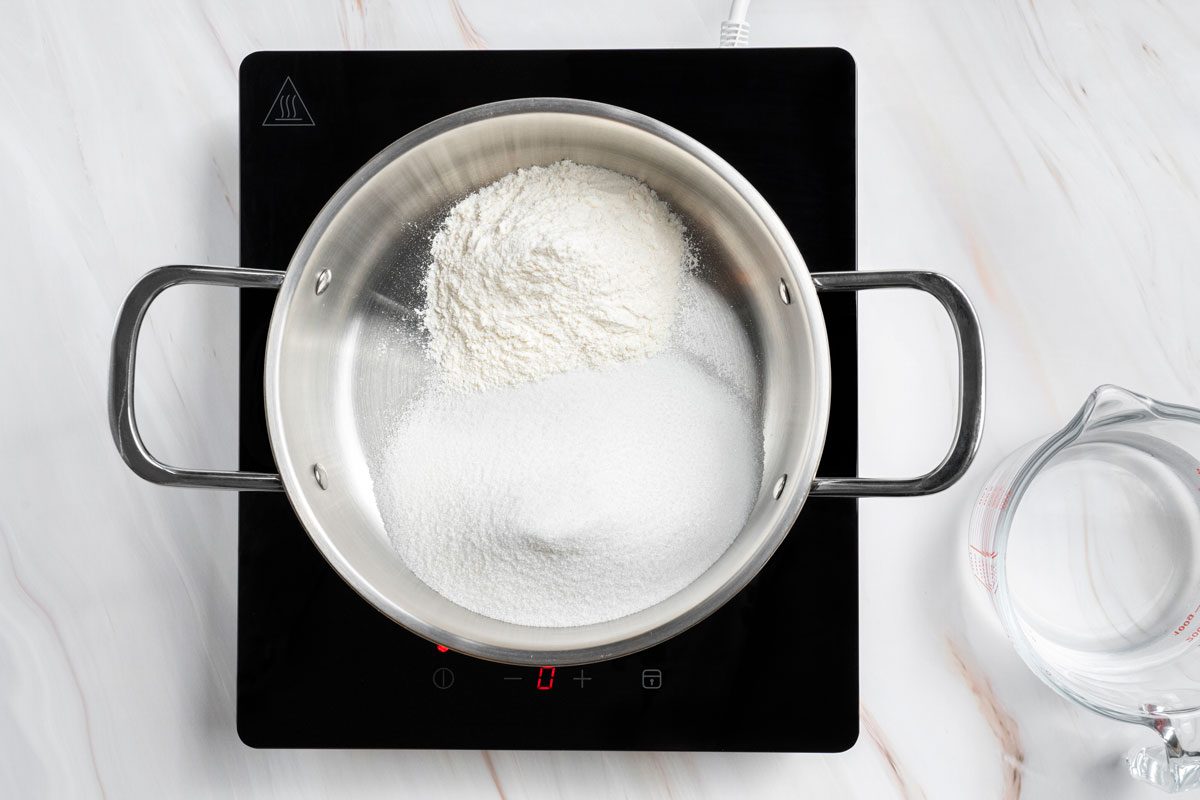 Overhead shot of a large saucepan combine sugar and flour over a induction; arranged on a marble surface;