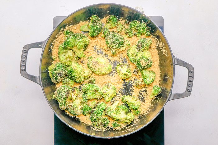 A pan filled with broccoli florets topped with grated cheese or bread crumbs, sitting on a black stovetop.