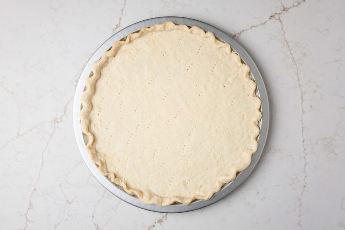 Overhead shot of roll out into a 14 inch circle; Place on an ungreased 12 inch pizza pan; Flute edges to form a rim; prick bottom of crust; Bake at 350 degree for 15 minutes; all set on a white texture marble surface