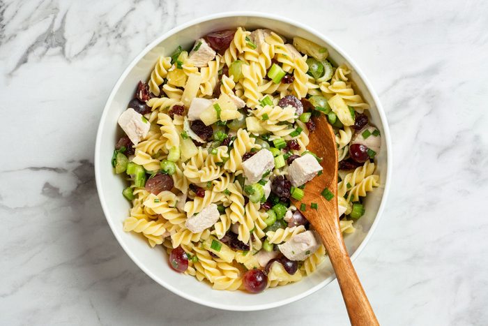 Overhaeds hot of stir pasta into chicken mixture; wooden spoon; all set on a marble surface