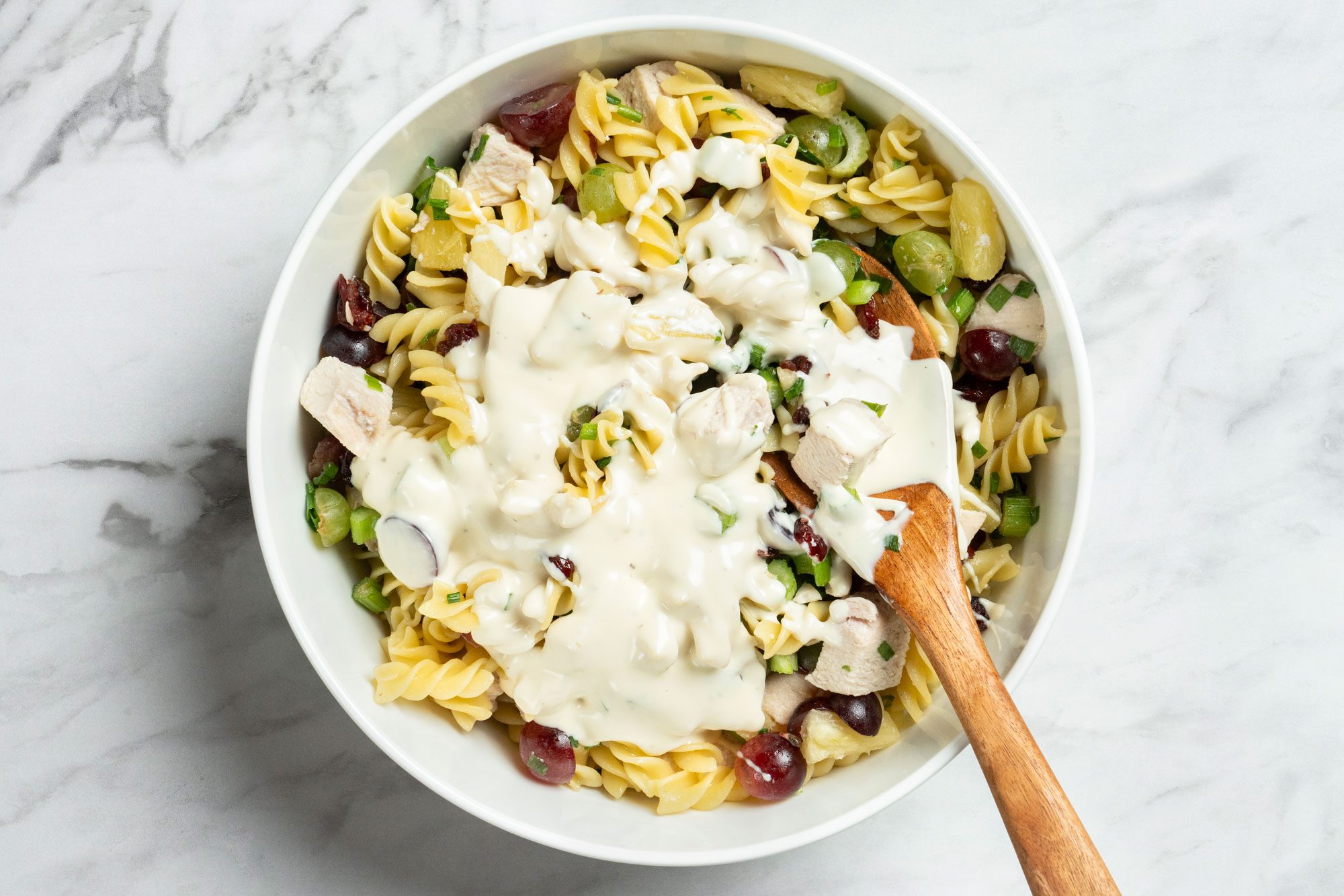 Overhead shot of pour over salad and toss to coat; Cover and refrigerate for at least 1 hour; wooden spoon; all set on a marble surface