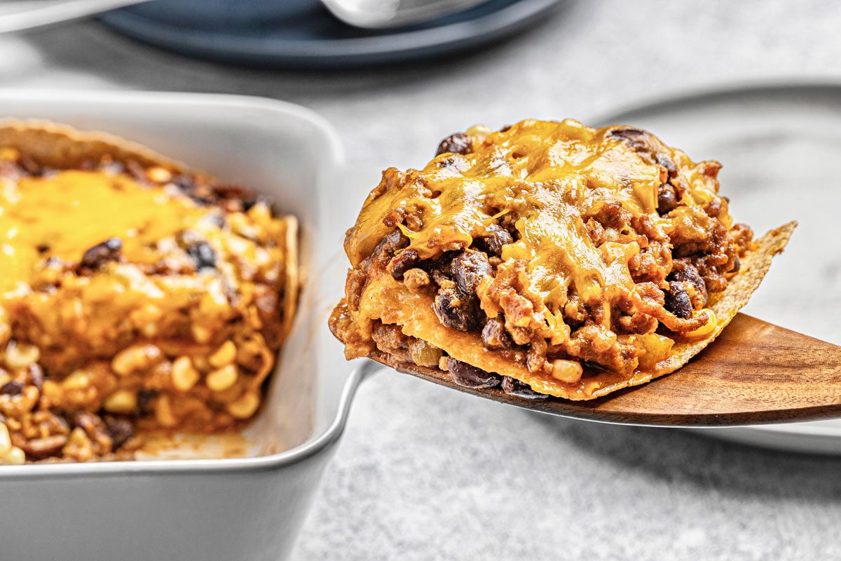 close up shot of a Chili Bake with black beans, corn, and ground meat, being served from a white baking dish with a wooden spatula