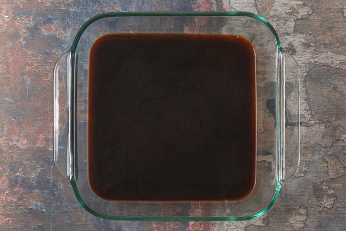 overhead shot of a glass baking dish filled with a dark coffee, placed on a textured surface with shades of blue, brown, and gray