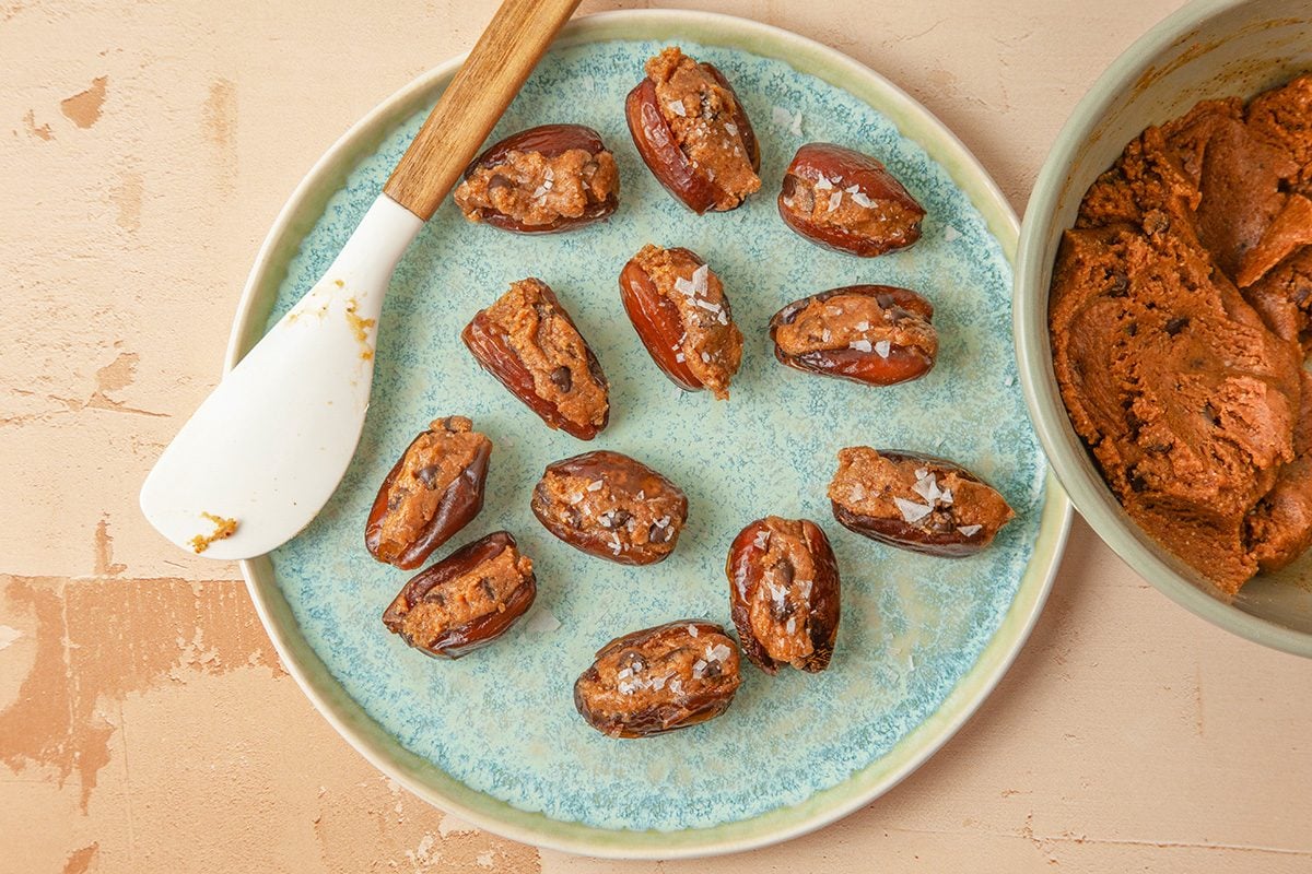 Overhead shot of spoon a generous teaspoon of dough into each date; Refrigerate 10 minutes; all set on a light orange background;