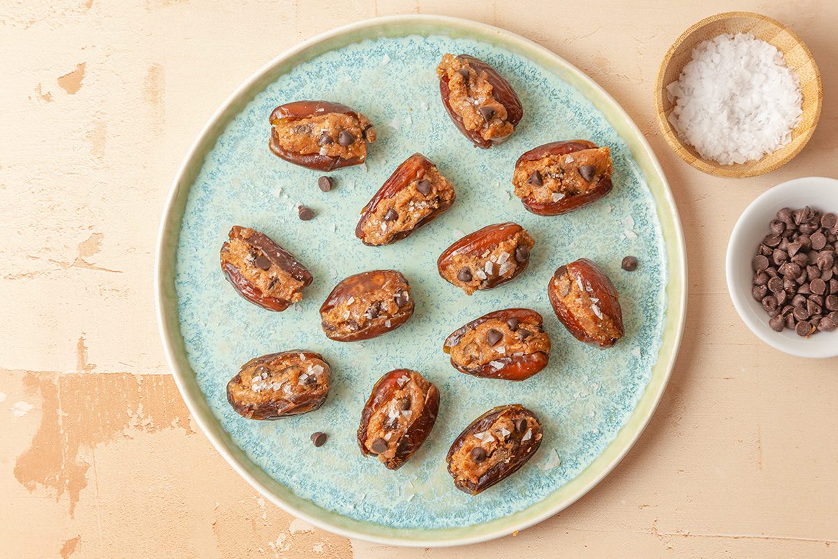 Overhead shot of Cookie Dough-Stuffed Dates; served ona ceramic plate; garnish with flaky sea salt just before serving; all set on a light orange background;