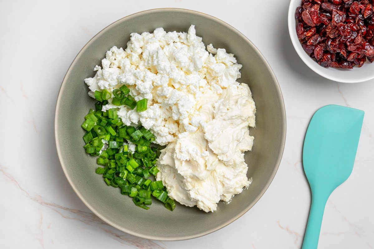 Overhead shot of a small bowl combine the cream cheese, feta cheese and onions; all set on a white marble surface;