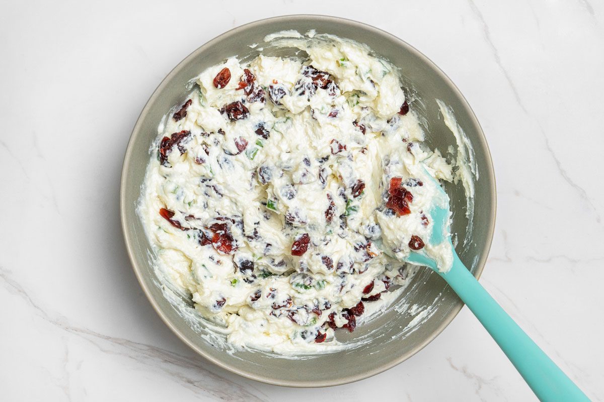 Overhead shot of stir in cranberries; spatula; all set on white marble surface;