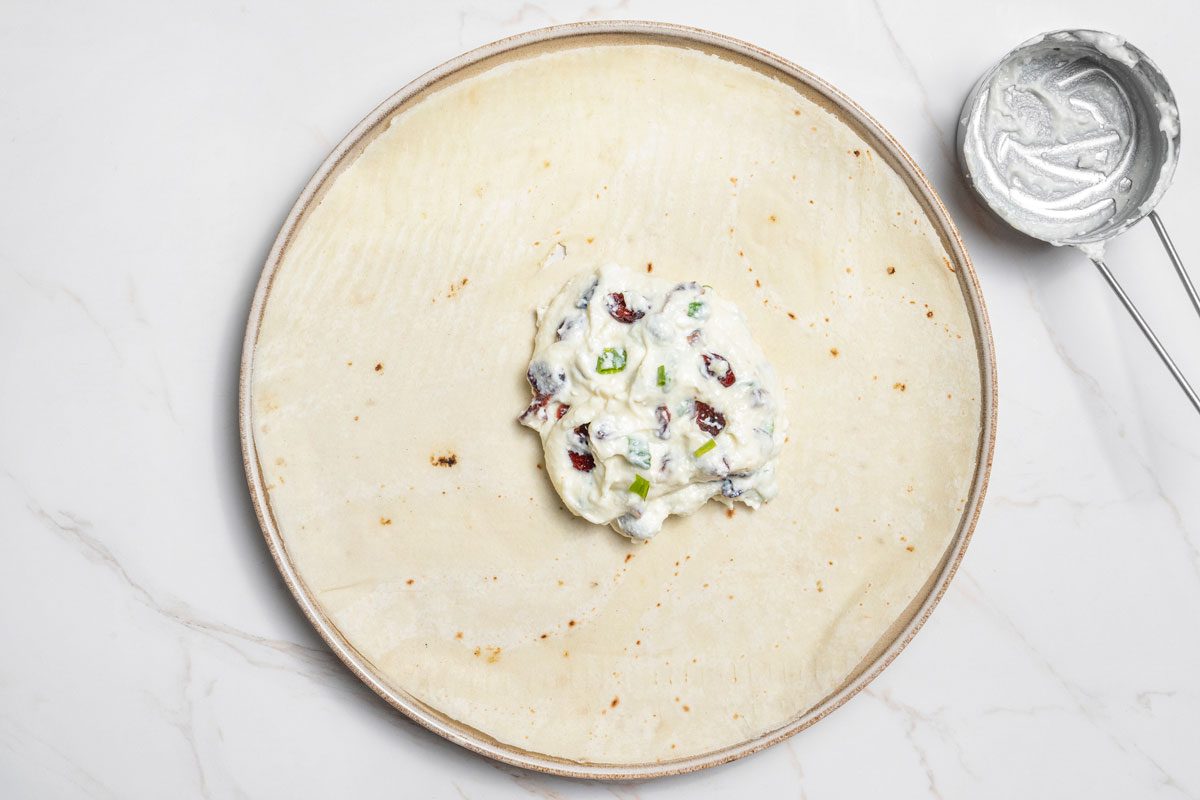 Overhead shot of spread about 1/2 cup mixture over each tortilla all set on a white marble surface;