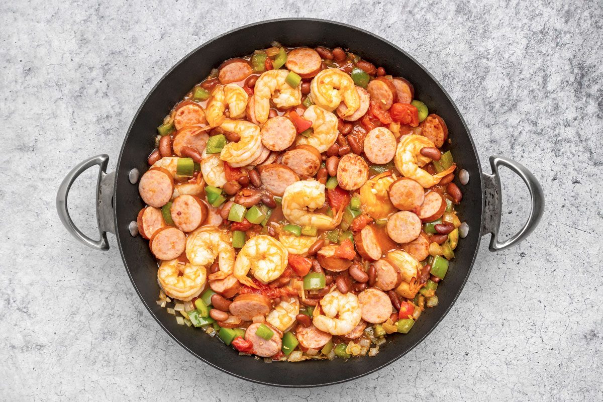 In the same skillet saute onion and green pepper in remaining oil until tender; Add garlic; beans; tomatoes; shrimp; Worcestershire sauce; sausage and remaining Creole seasoning