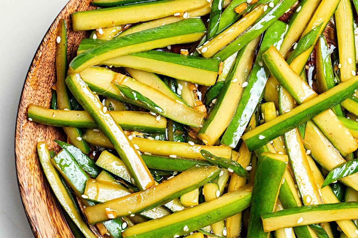 Sliced cucumber sticks tossed with sesame seeds and a glossy dressing, served in a wooden bowl.