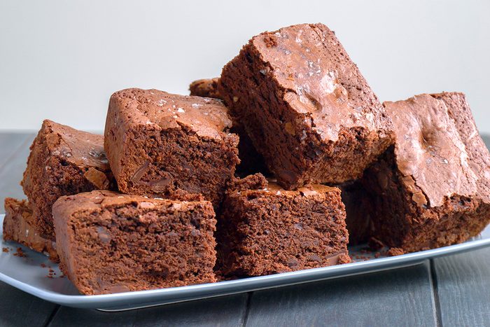 A plate piled with thick, square chocolate brownies, featuring a crackly top and rich, fudgy texture, set on a gray wooden surface.