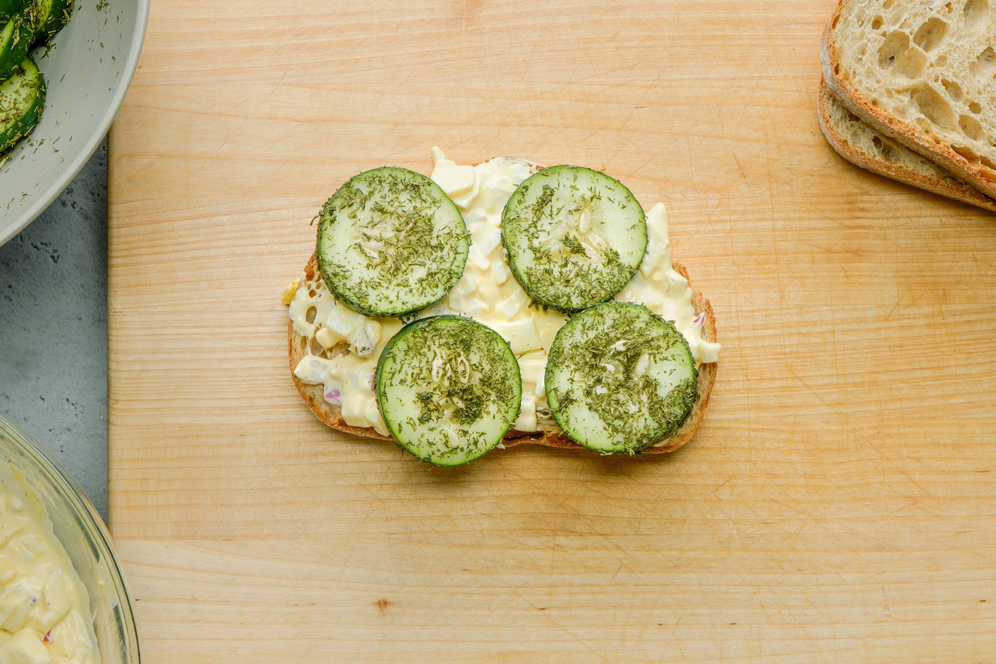 Overhead shot of top with cucumbers and remaining toast, arranged on a wooden board; all set on a grey surface