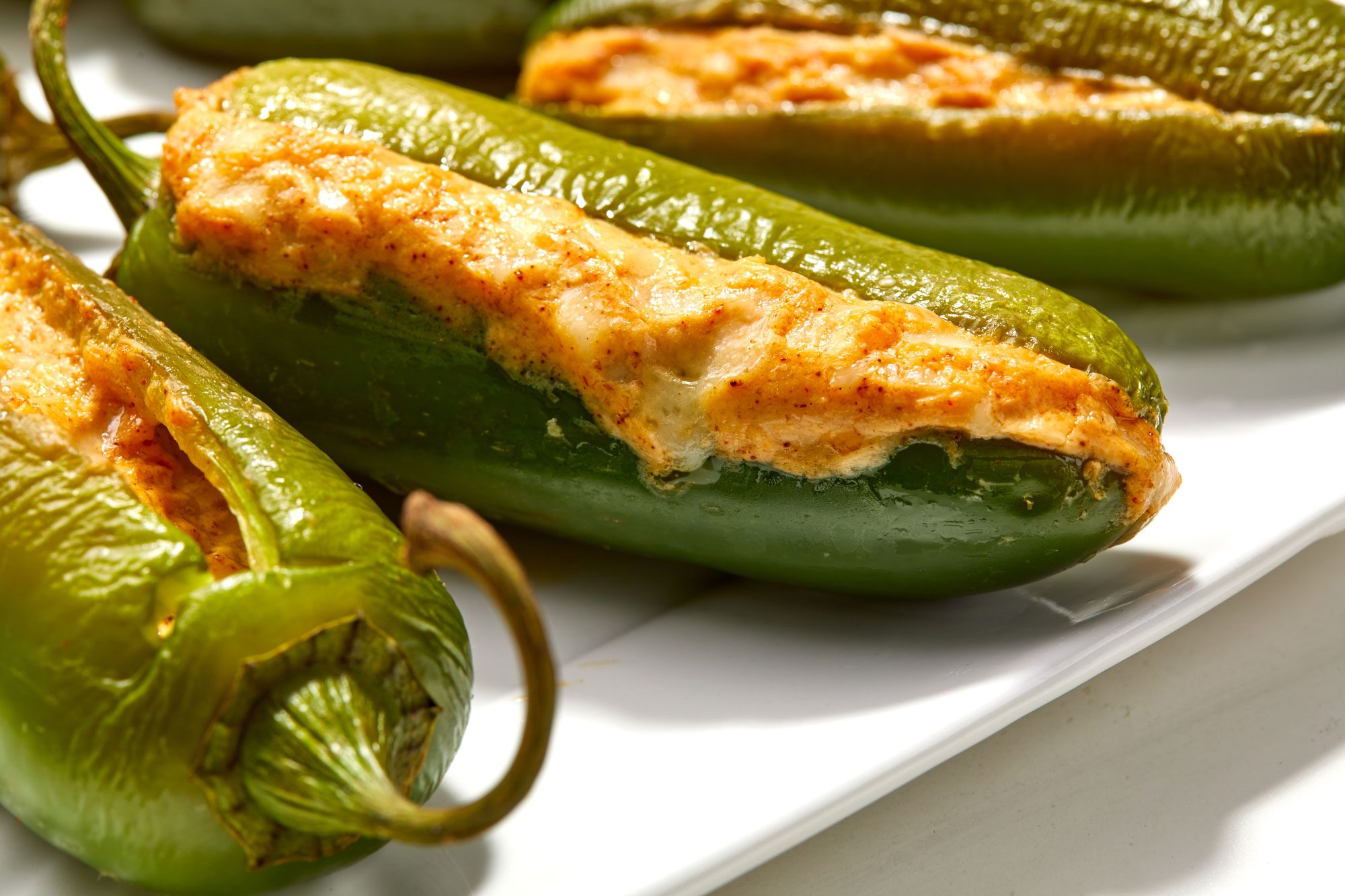 Closeup shot of Grilled Stuffed Jalapenos serve warm on a large white platter; all set on a white surface