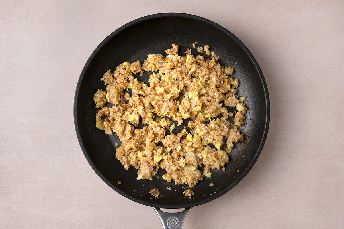 Cooked, crumbled ground meat mixed with small pieces of vegetables in a black frying pan, placed on a light beige surface.
