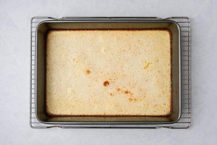 A top shot of a rectangular baking pan holds golden-brown baked custard on a cooling rack; the setup rests on a light surface, suggesting freshness and homemade comfort
