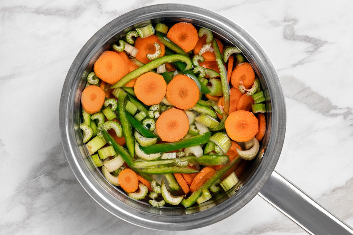 celery, carrots and green pepper submerged in water in a large saucepan 