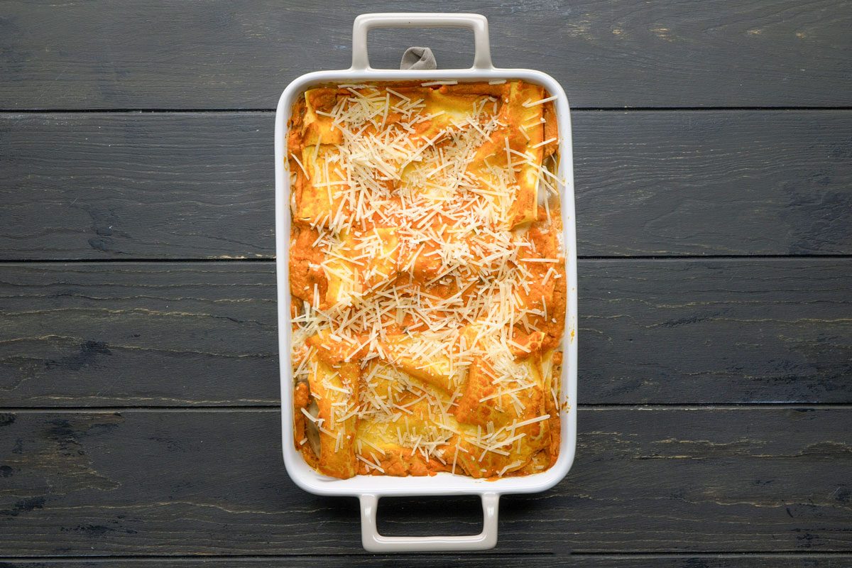 Top Shot of a The white rectangular baking dish contains baked ravioli covered in melted cheese; sitting on a dark wooden surface; presenting a hearty and inviting meal setting