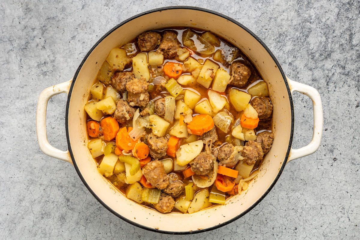 Overhead shot of a Dutch oven over medium heat; brown sausage; drain; Add the water; potatoes; carrots; celery; onions; Worcestershire sauce and seasonings; Bring to a boil; Reduce heat; cover and cook over low heat for 1 hour or until sausage is no longer pink and vegetables are tender; on a grey marble surface;