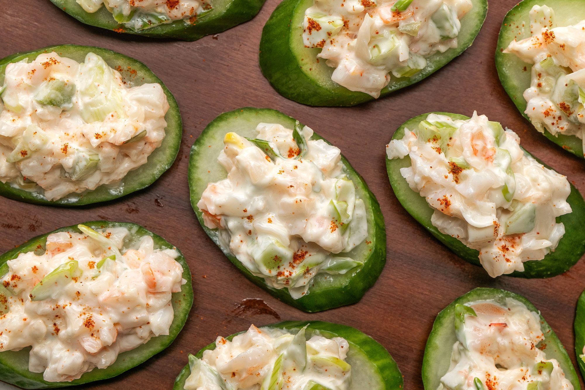 Overhead shot of Shrimp and Cucumber Rounds served on a dark brown wooden tray; set on a marble surface