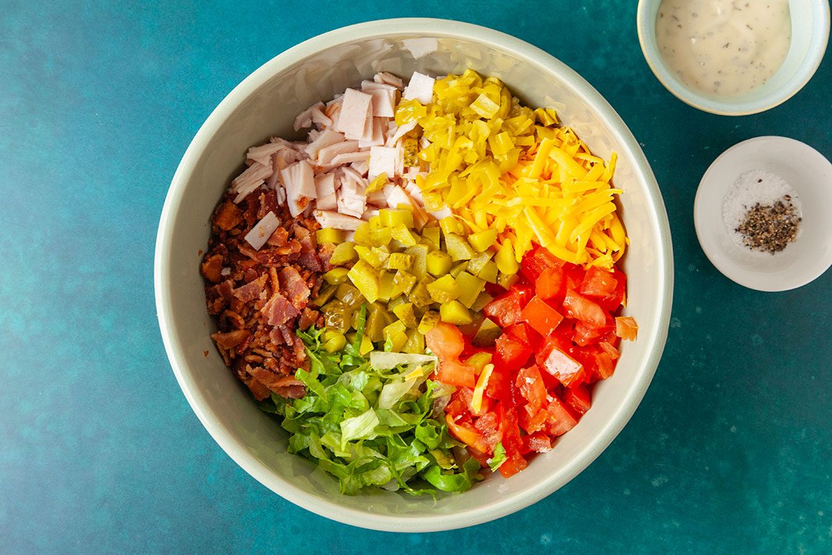 Copped romaine lettuce, tomato, turkey, bacon, pickles and banana peppers with the shredded cheese in a large bowl