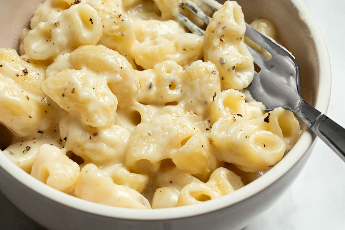 A bowl of creamy macaroni and cheese topped with cracked black pepper, with a fork resting inside the bowl.