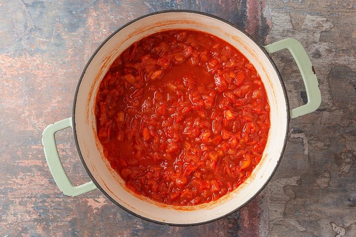 This is a top-down shot showing a pot of chunky red tomato sauce with visible tomato and onion pieces; the light green handles contrast with the white interior; background features a rustic; textured surface