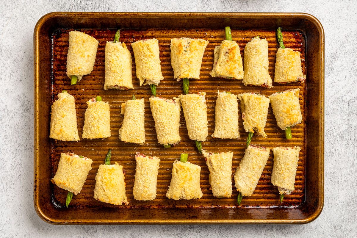 Overhead shot; a baking sheet displays golden brown breaded rolls with green vegetable filling; evenly spaced