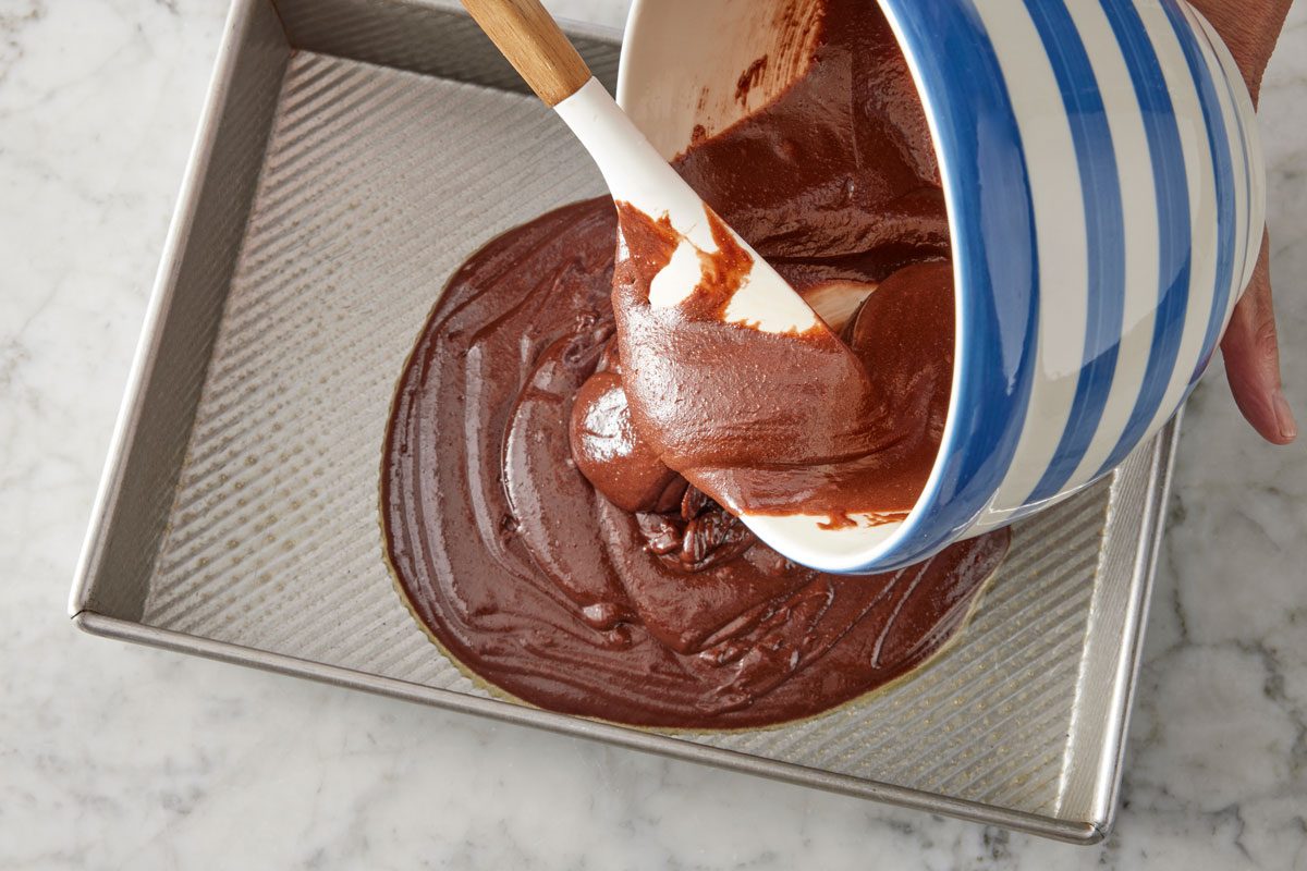 transferring brownie mix in a pan with the help of spatula