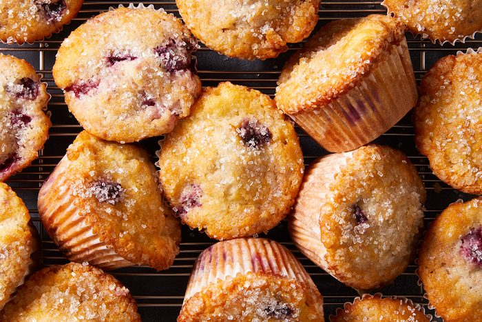 A close-up of several golden-brown blueberry muffins on a cooling rack, topped with a sprinkling of coarse sugar.