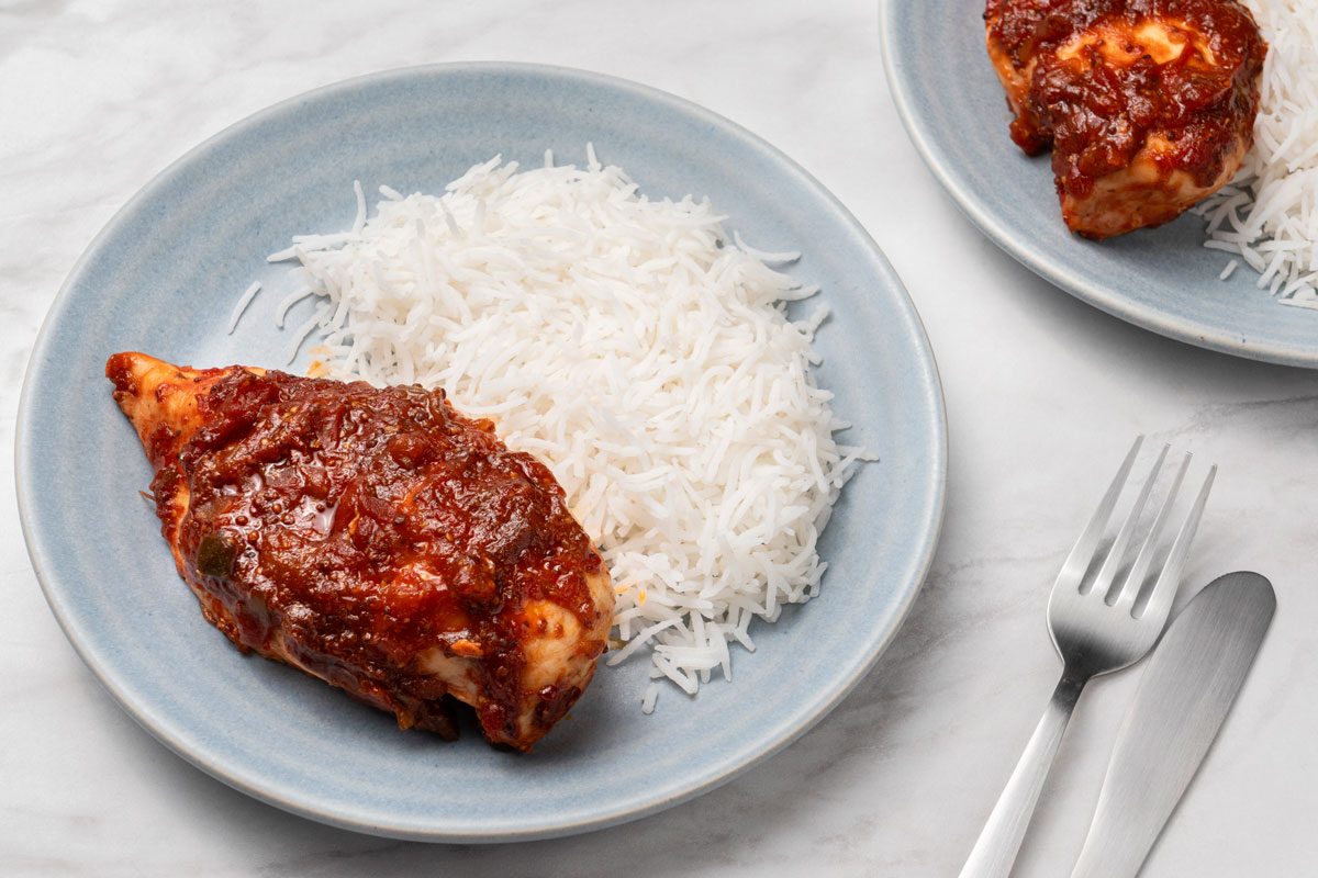 High angle shot of Chicken Picante served with rice on two light blue ceramic plates; Fork and knife placed on a marble surface;