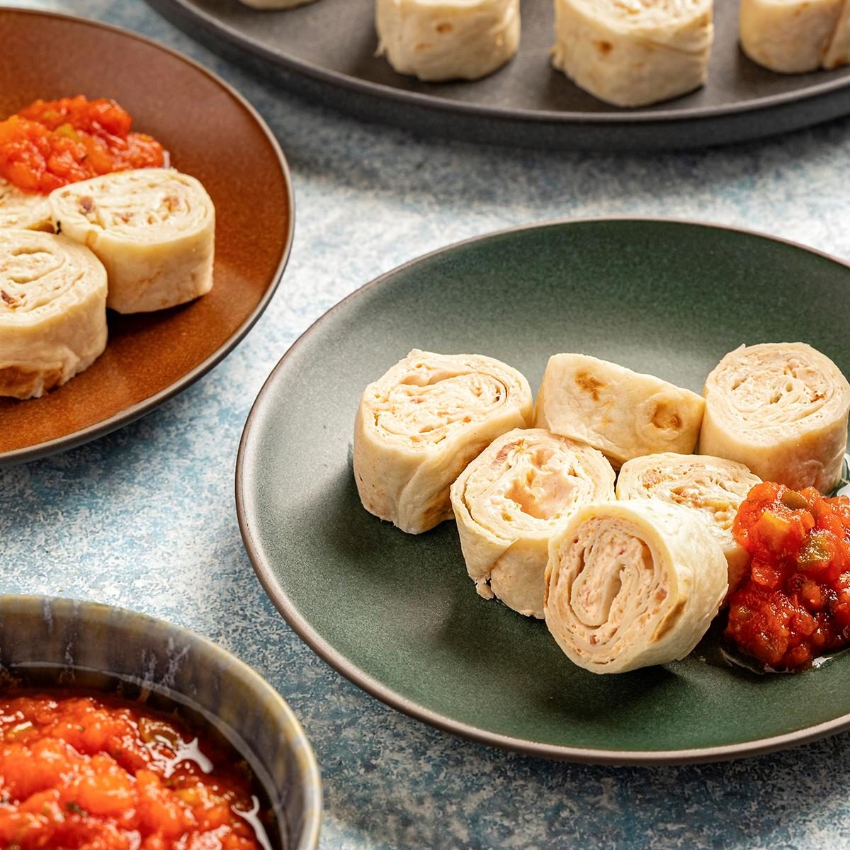 Overhead shot; sliced tortilla pinwheels on plates; layered filling visible; served with chunky tomato salsa
