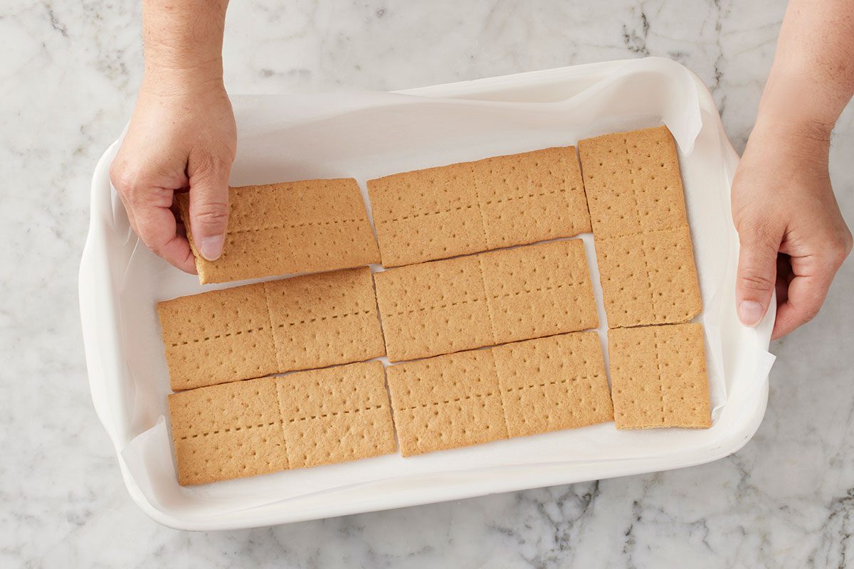 a layer of graham crackers being placed over the bottom of the lined dish