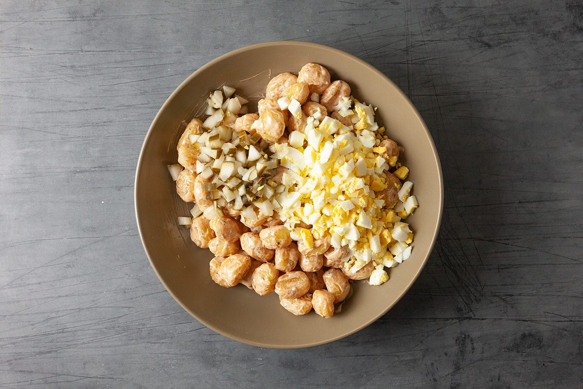 A brown bowl on a gray surface contains chopped hard-boiled eggs, diced pickles, and chunks of cooked soy protein.
