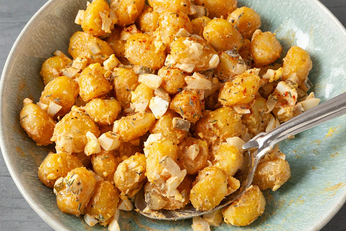 A bowl filled with roasted chickpeas mixed with chopped onions and herbs, with a spoon resting in the bowl. The chickpeas appear golden and seasoned.