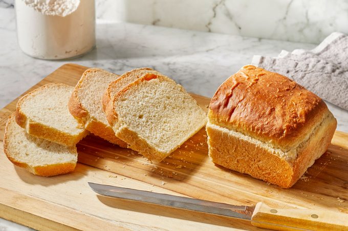Few pieces of bread cut from a whole bread and placed on a wooden board