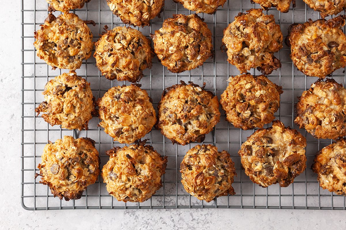 Freshly baked oatmeal cookies with chocolate chips cooling on a wire rack, arranged in neat rows on a light-colored tabletop.