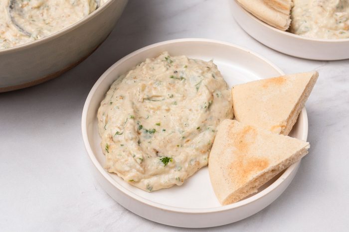 3/4 angle view shot of Mediterranean Eggplant Dip served with flat braeds on white plates; all set on a marble surface;