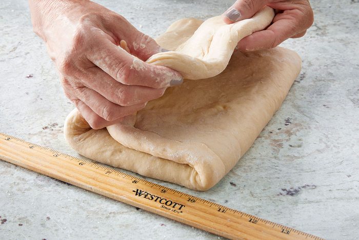 Close shot of a person folding a sheet of dough on a floured surface beside a wooden ruler.