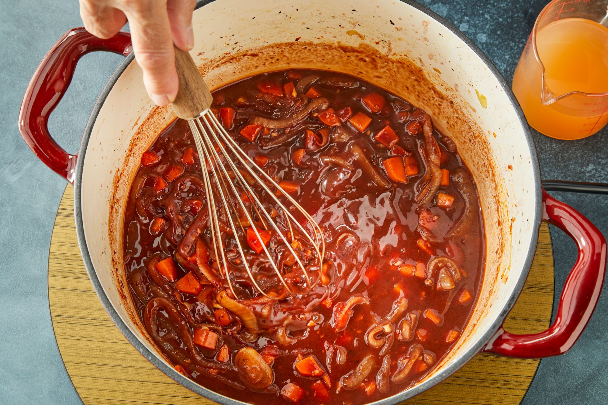 Overhead shot of dutch over; cook until sauce begins to thicken 1-2 minutes; whisk tool; induction; dark surface;