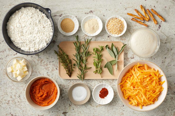 Ingredients for Pumpkin Shaped Rolls in big and small bowls and on wooden board on a counter.