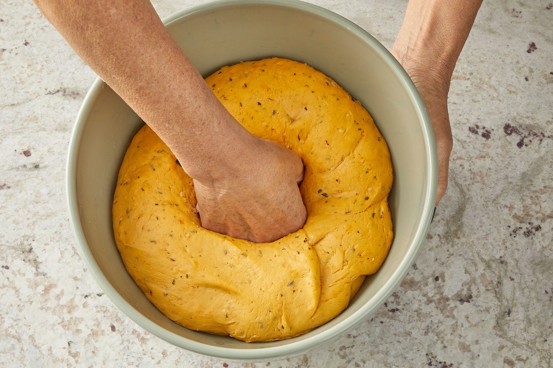 Punching the kneaded dough in a green bowl to deflate the air in it.