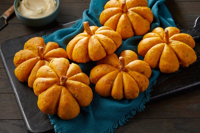 Pumpkin Shaped Rolls on a blue kitchen cloth in a dish with butter on side in a bowl.