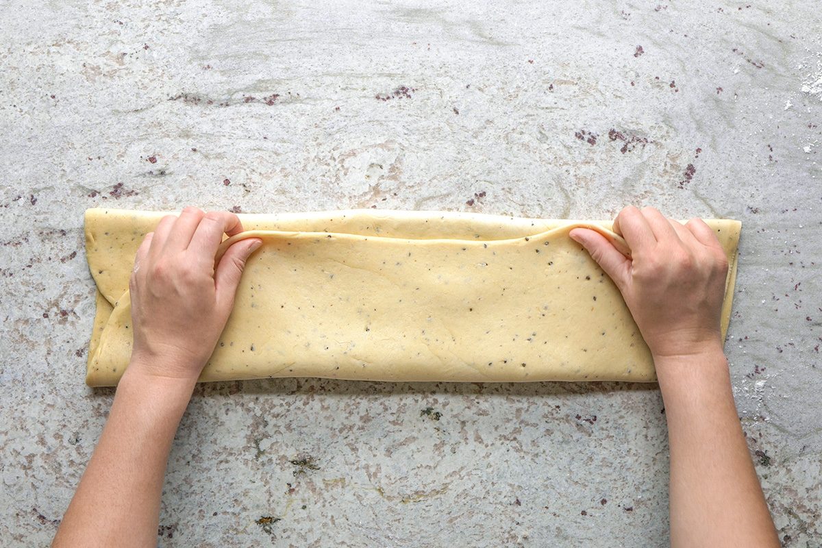 overhead shot of Two hands folding a rectangular sheet of dough on a lightly floured surface, preparing it for baking