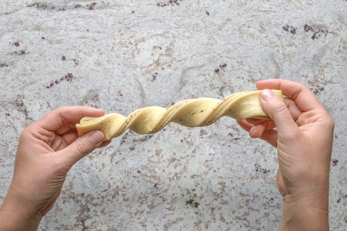 overhead shot of Two hands holding a twisted strip of dough over a light, speckled countertop