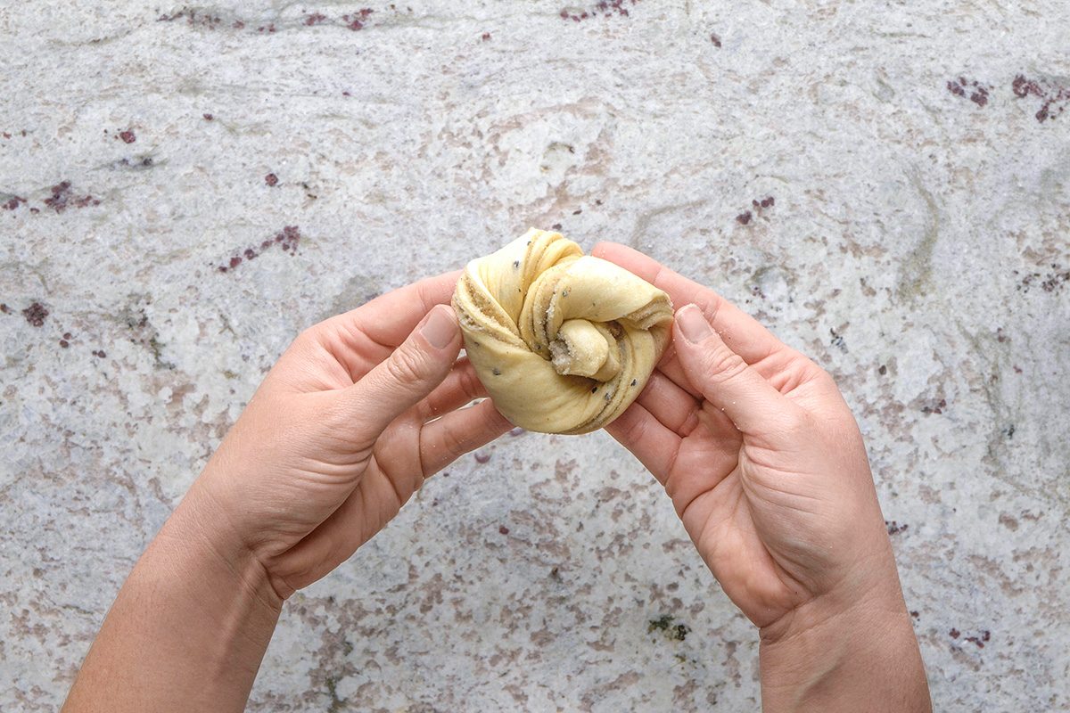 overhead shot of Two hands holding a twisted, unbaked pastry knot over a light, speckled countertop