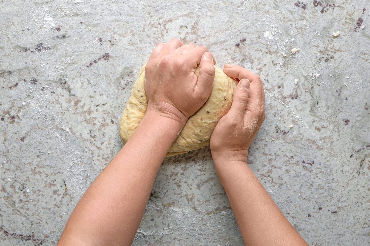 overhead shot of Two hands knead a ball of dough on a lightly floured, textured surface