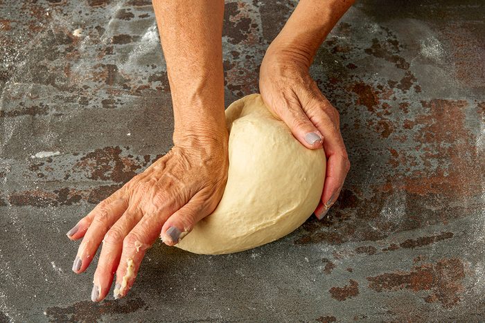 Overhead shot of a pair of hands kneading a ball of dough on a floured dark countertop