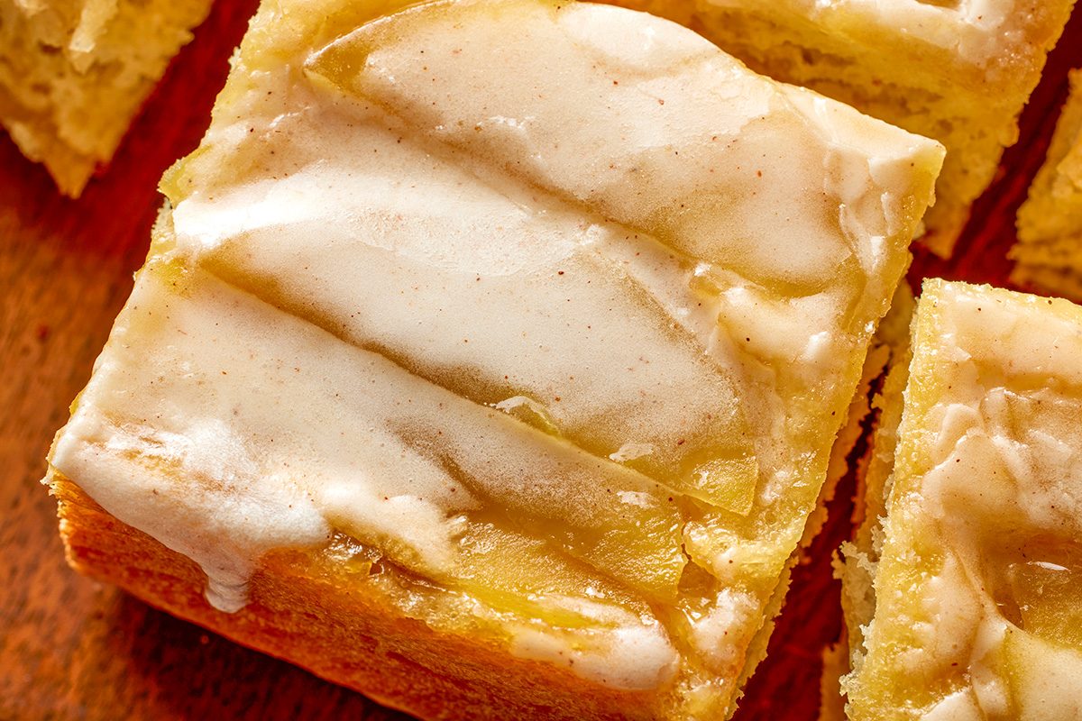 Overhead close-up shot of a piece of Upside Down Apple Bread, a glazed yellow cake with shiny; slightly cracked icing on top; resting on a wooden surface