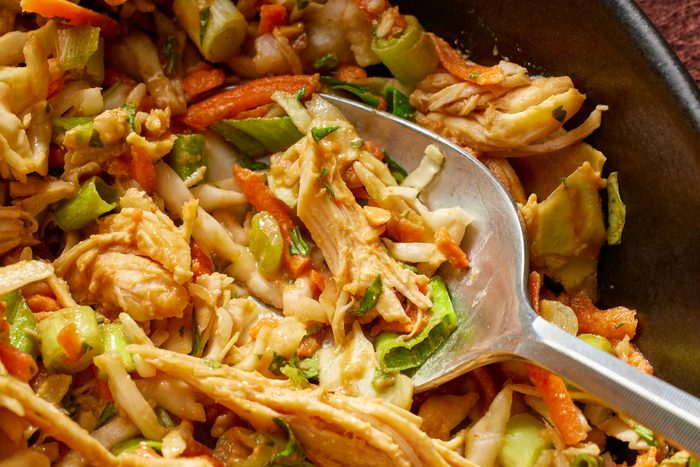 Close-up shot of Thai Chicken Coleslaw in a large bowl with cabbage, carrots, and green onions, with a silver spoon;