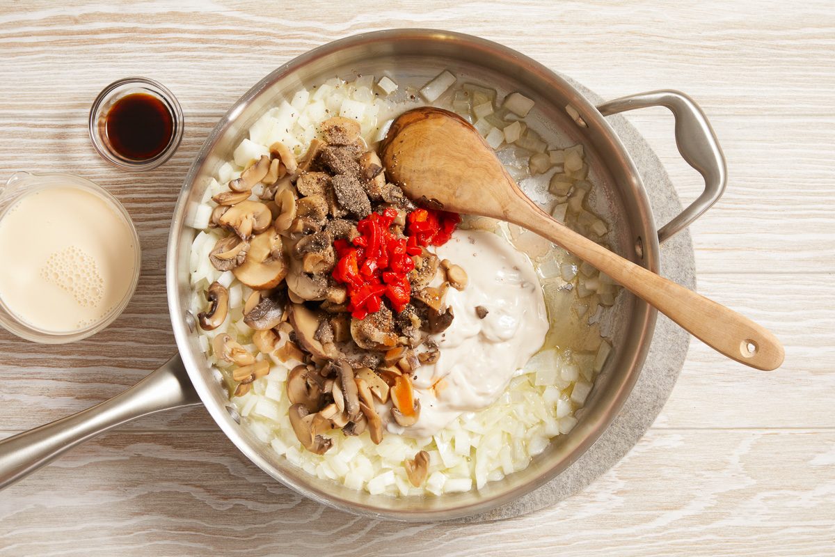 condensed soup, mushrooms, milk, pimientos, soy sauce, black pepper and hot pepper sauce being cooked with onions in melted butter